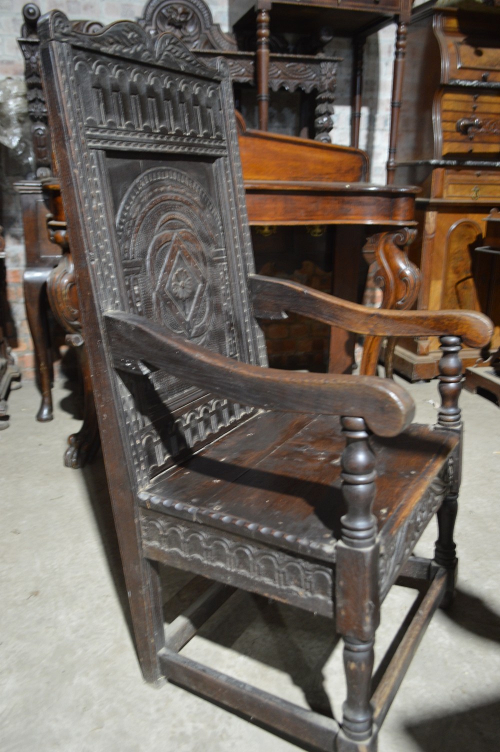 A dark carved oak wainscot armchair featuring a detailed arched panel back, turned front legs, and sturdy stretchers. View IV