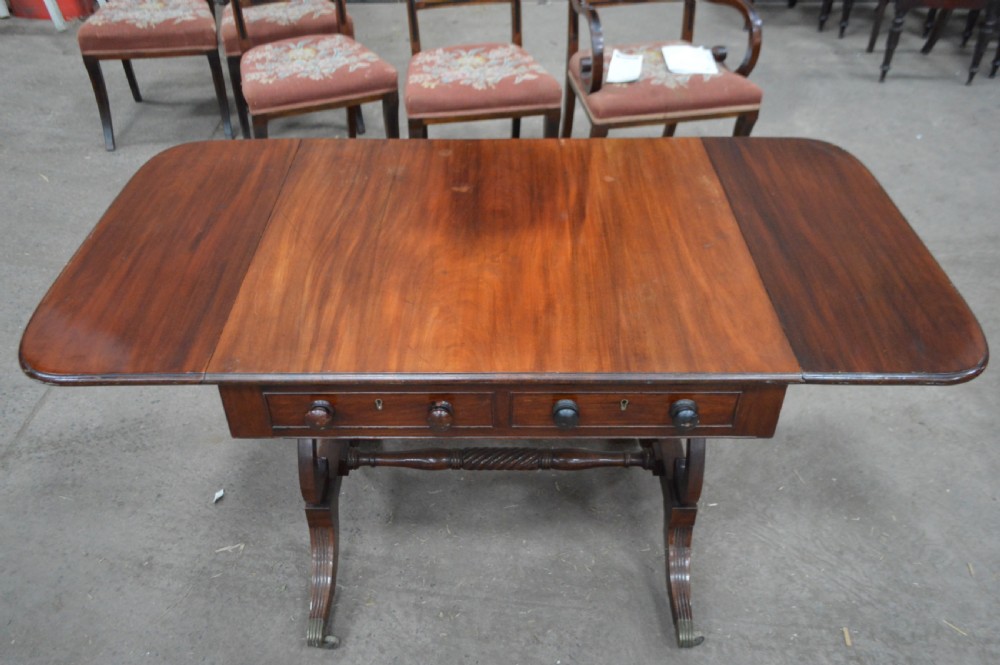 A Georgian mahogany sofa table featuring twin drop leaves, two front drawers with round wooden knobs, a turned cross-stretcher, and splayed legs ending in brass caps. View III