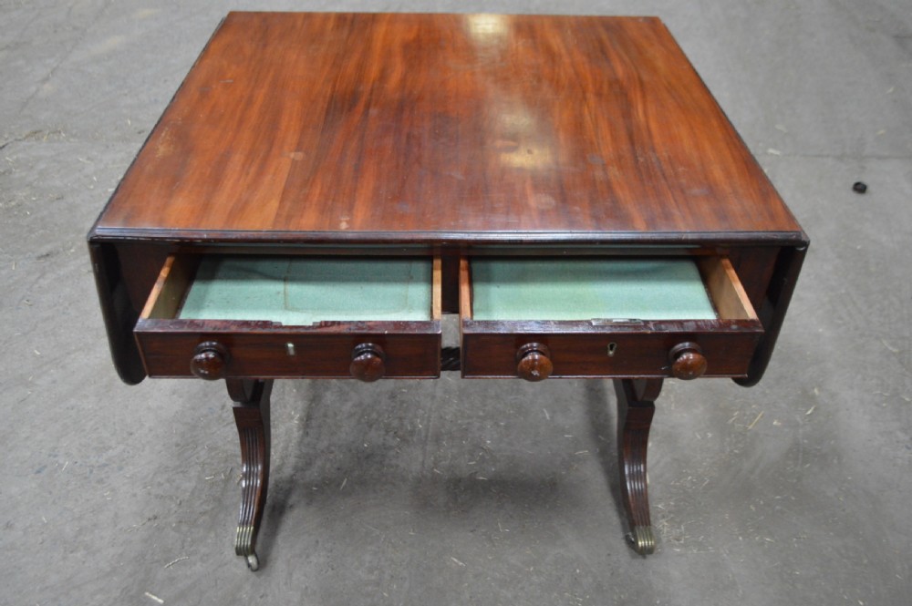 A Georgian mahogany sofa table featuring twin drop leaves, two front drawers with round wooden knobs, a turned cross-stretcher, and splayed legs ending in brass caps. View V