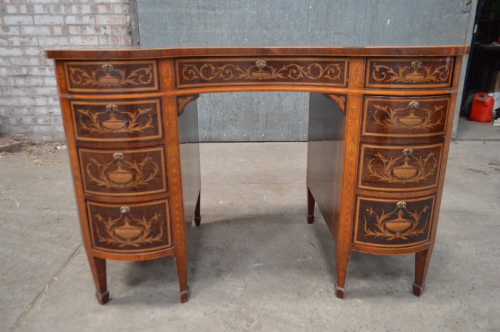 A mahogany kidney-shaped writing desk decorated with intricate marquetry urn inlays, nine drawers, and square tapered legs.