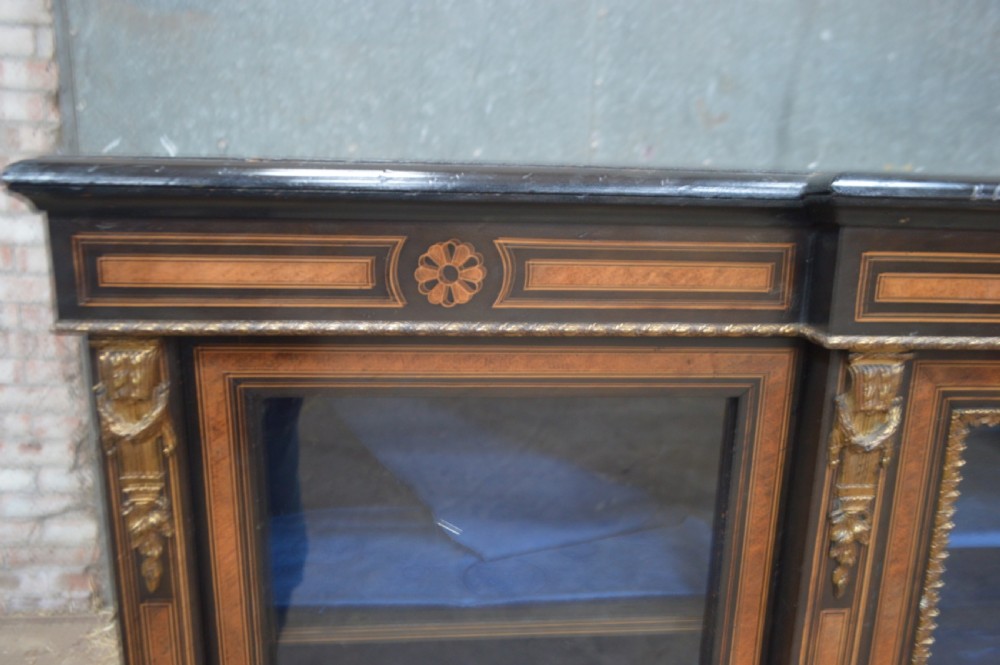 A Victorian ebonised and amboyna three-door breakfront glazed bookcase featuring intricate inlays, brass mounts, and a blue-lined interior. View II