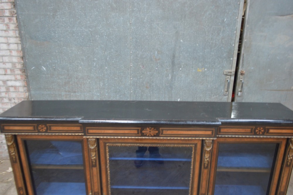 A Victorian ebonised and amboyna three-door breakfront glazed bookcase featuring intricate inlays, brass mounts, and a blue-lined interior. View III