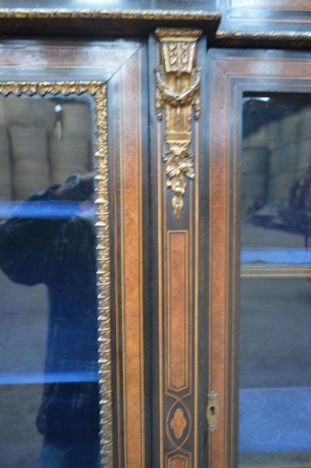 A Victorian ebonised and amboyna three-door breakfront glazed bookcase featuring intricate inlays, brass mounts, and a blue-lined interior. View V