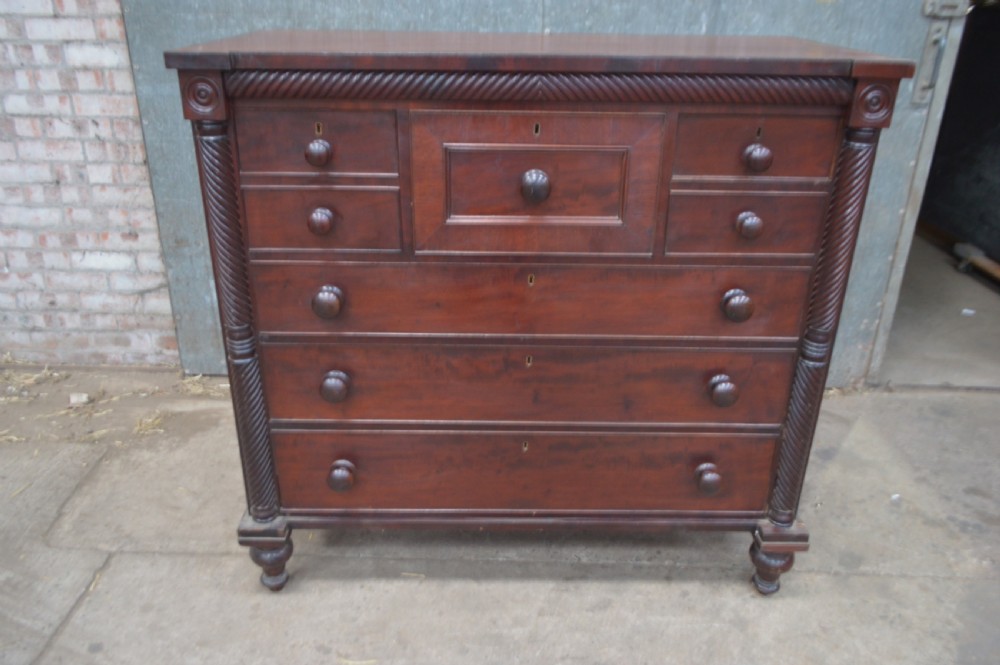A Scottish Regency mahogany chest of drawers featuring rope-twist columns, corner rosettes, a central bonnet drawer, and turned feet.