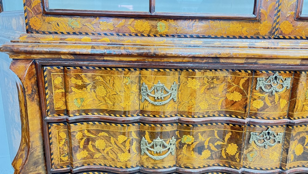 A Dutch walnut display cabinet featuring intricate floral marquetry inlay throughout, an arched glazed upper section, a shaped lower chest with drawers, and carved claw feet. View IX