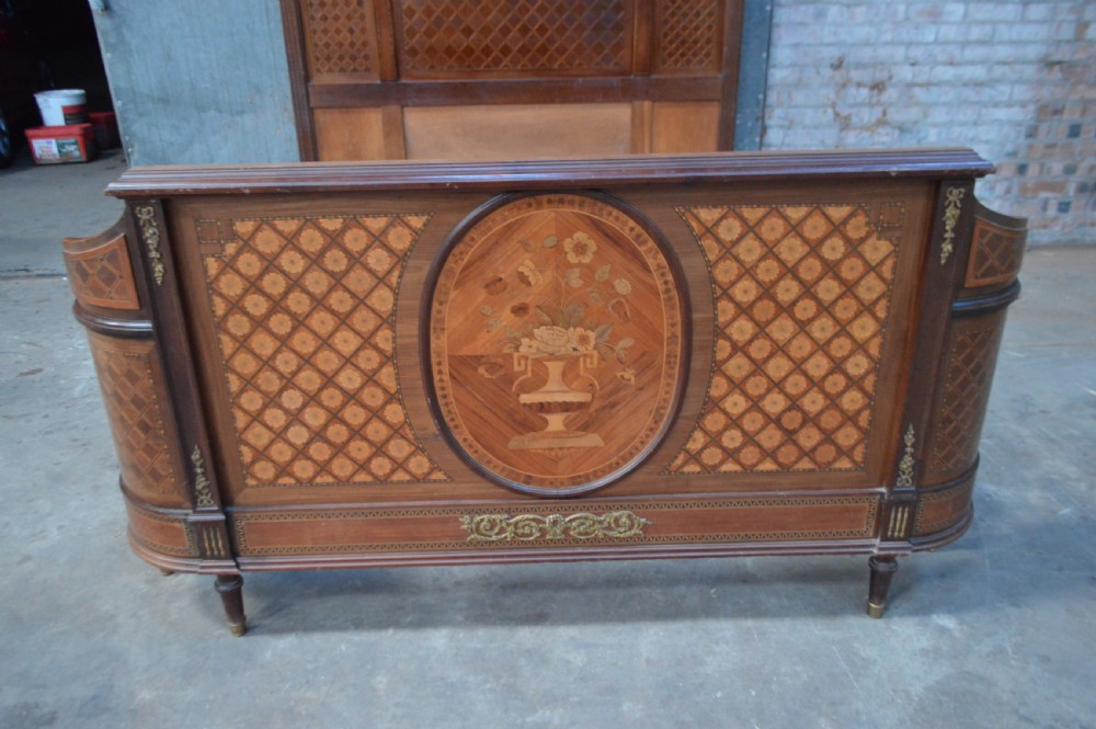 A French Louis XVI Revival wooden double bed featuring intricate floral marquetry paneling, trellis parquetry, curved footboard ends, and gilded metal mounts. View X
