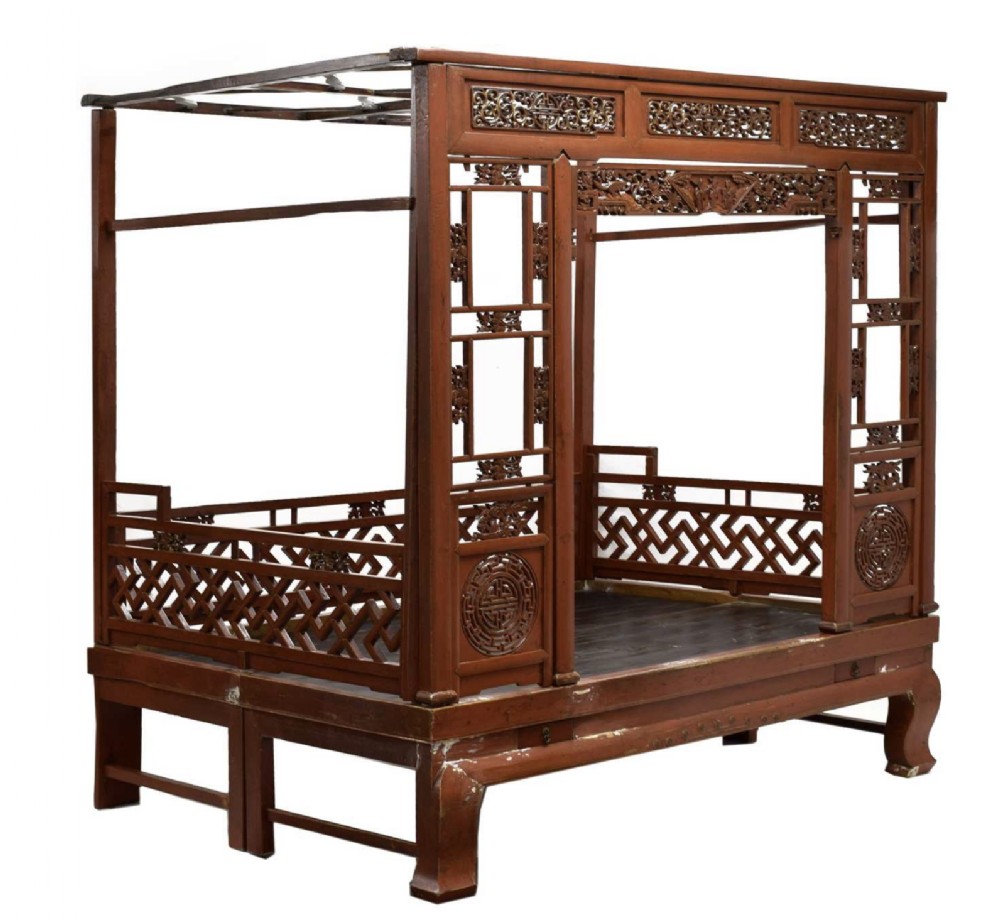 A 19th-century Chinese red lacquered wooden marriage bed featuring a full canopy frame, carved lattice railings, and pierced relief panels.