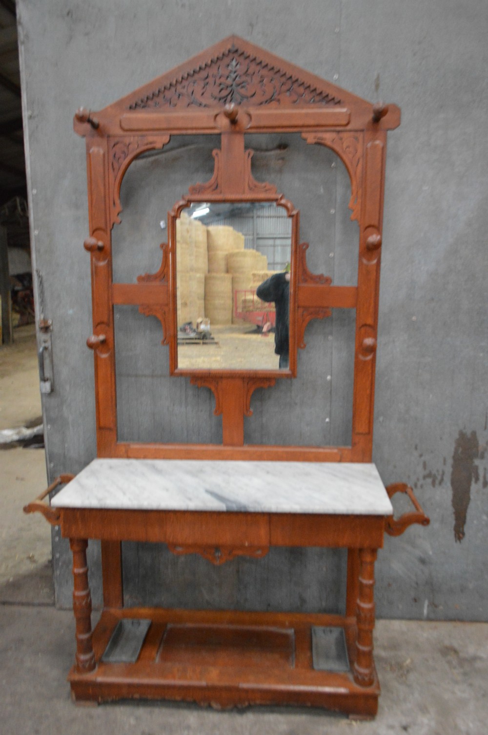 A Victorian oak hall stand featuring a central mirror, carved top pediment, coat pegs, a white marble console surface, and a lower shelf with umbrella drip trays.