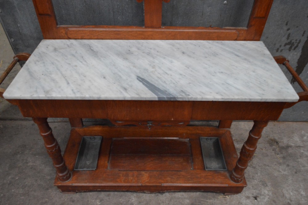 A Victorian oak hall stand featuring a central mirror, carved top pediment, coat pegs, a white marble console surface, and a lower shelf with umbrella drip trays. View II