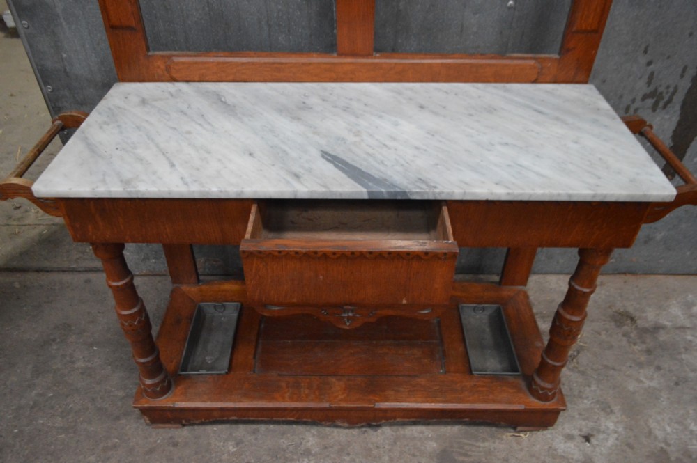 A Victorian oak hall stand featuring a central mirror, carved top pediment, coat pegs, a white marble console surface, and a lower shelf with umbrella drip trays. View IV
