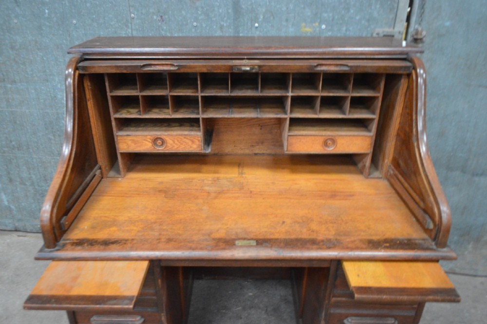 An open 1920s oak roll top desk featuring internal pigeonholes, two small drawers, and twin pedestal storage. View II