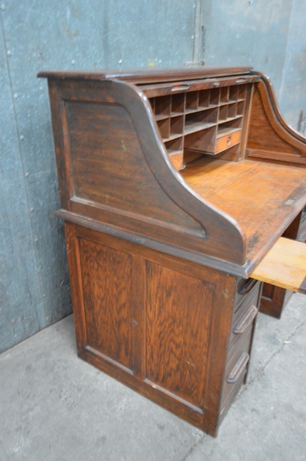 An open 1920s oak roll top desk featuring internal pigeonholes, two small drawers, and twin pedestal storage. View III