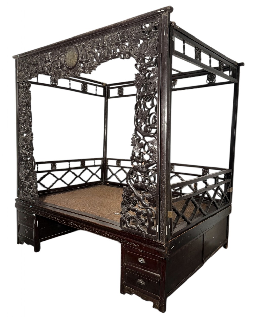 An antique 19th-century Chinese dark hardwood canopy bed with deeply carved floral top friezes, openwork lattice railings, and base drawers.