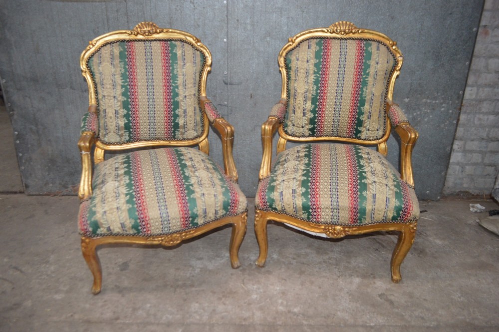 A pair of 19th-century French giltwood salon armchairs featuring carved crests, cabriole legs, and striped botanical woven fabric.