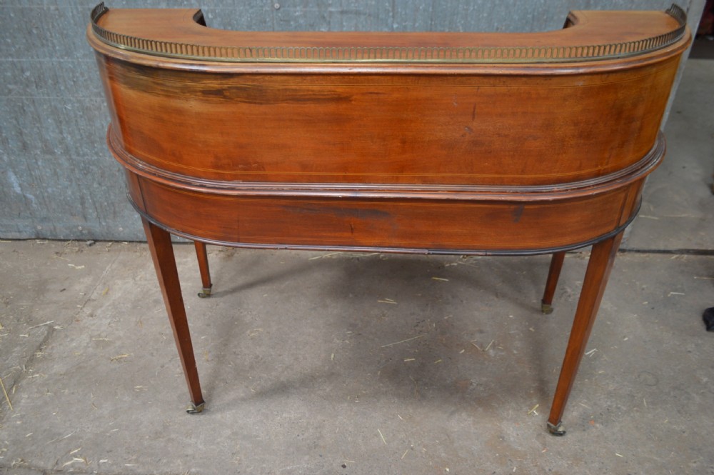 An Edwardian mahogany Carlton House desk featuring a raised U-shaped gallery of drawers, a brass rail, a green leather writing surface, and tapered square legs with castors. View III