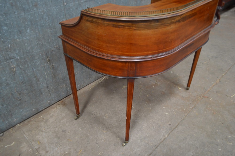 An Edwardian mahogany Carlton House desk featuring a raised U-shaped gallery of drawers, a brass rail, a green leather writing surface, and tapered square legs with castors. View V
