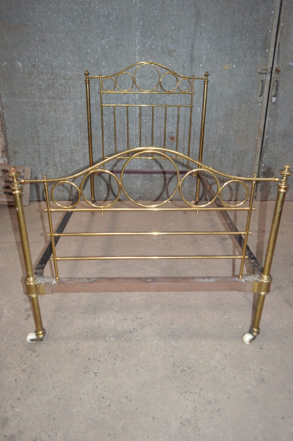 Victorian brass single bedstead featuring tubular brass posts with circular ring motifs, vertical spindles, and ceramic castors.