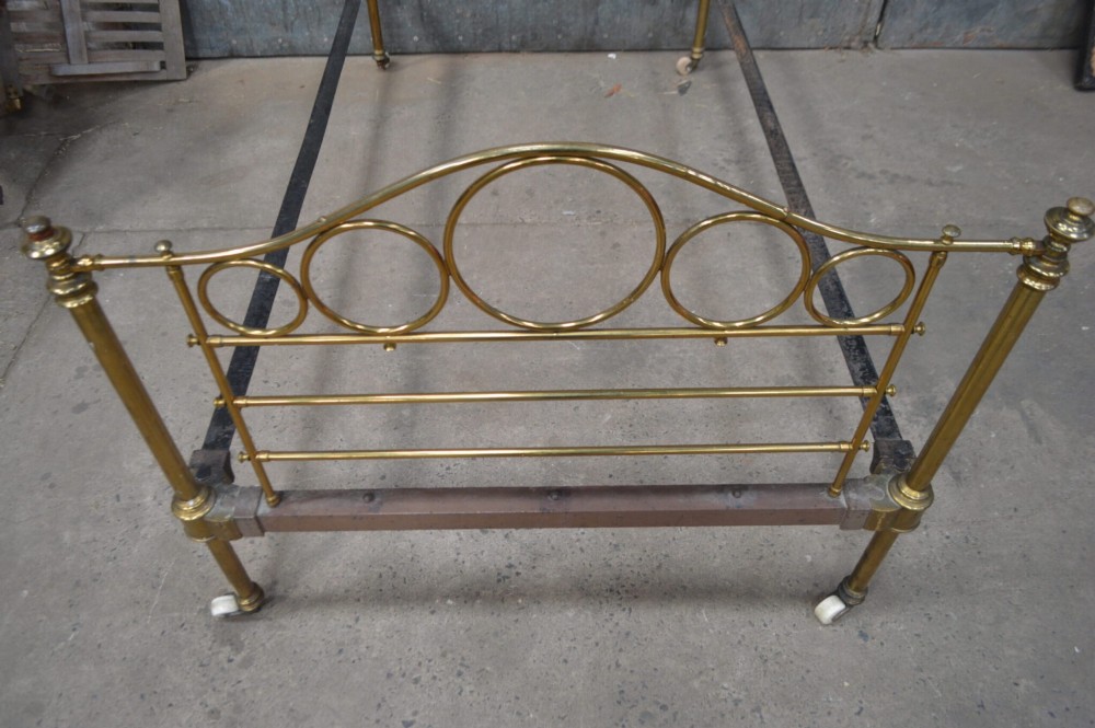 Victorian brass single bedstead featuring tubular brass posts with circular ring motifs, vertical spindles, and ceramic castors. View II