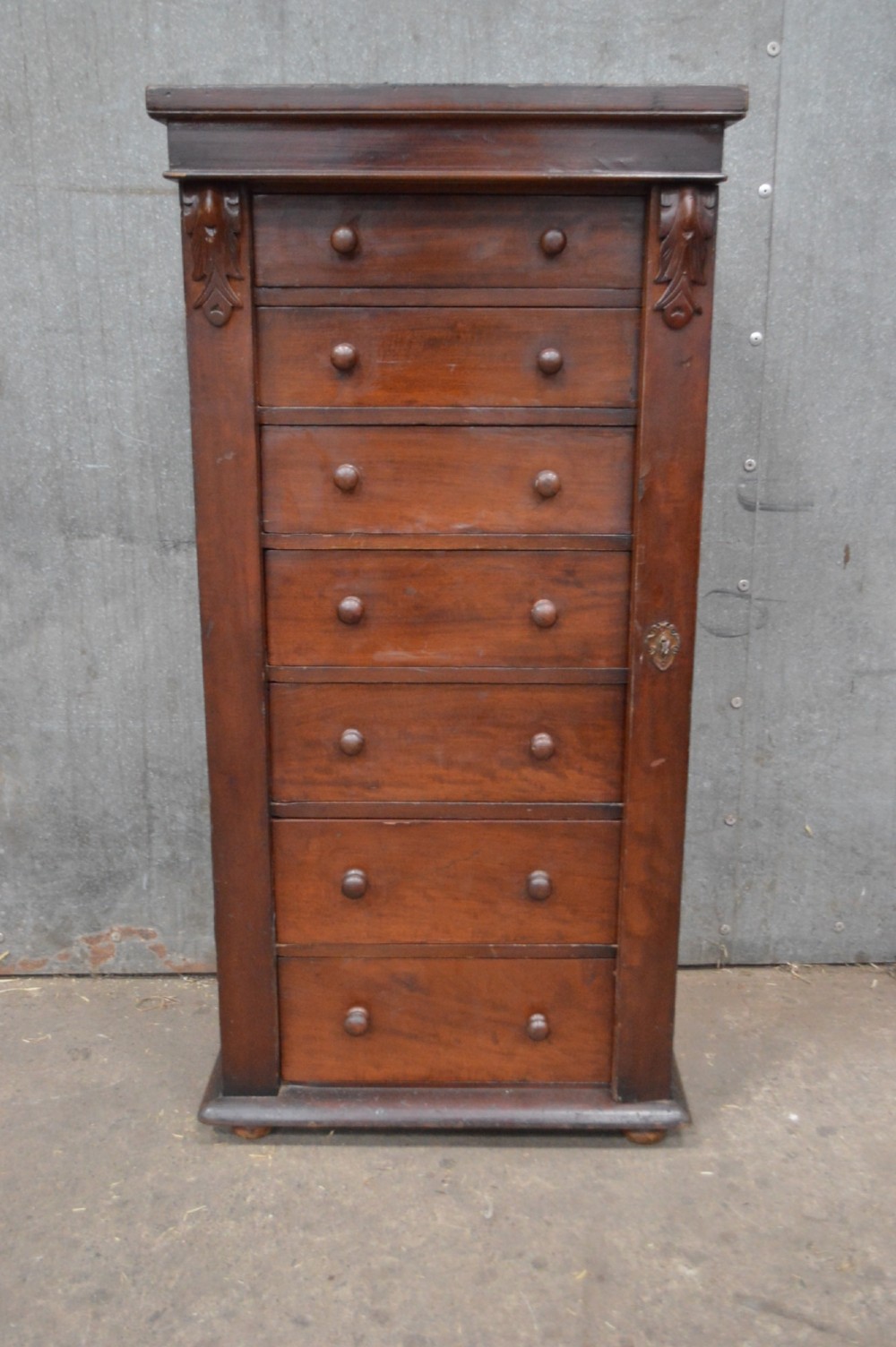 A tall, narrow Victorian mahogany Wellington chest featuring seven graduated drawers with turned wooden knobs and a hinged right-hand locking bar.