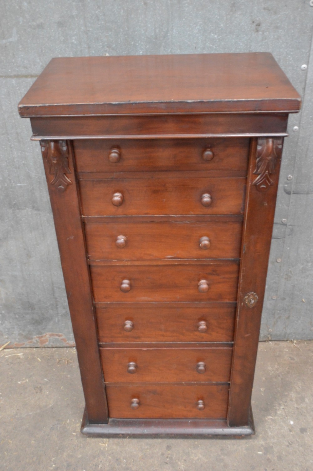A tall, narrow Victorian mahogany Wellington chest featuring seven graduated drawers with turned wooden knobs and a hinged right-hand locking bar. View II
