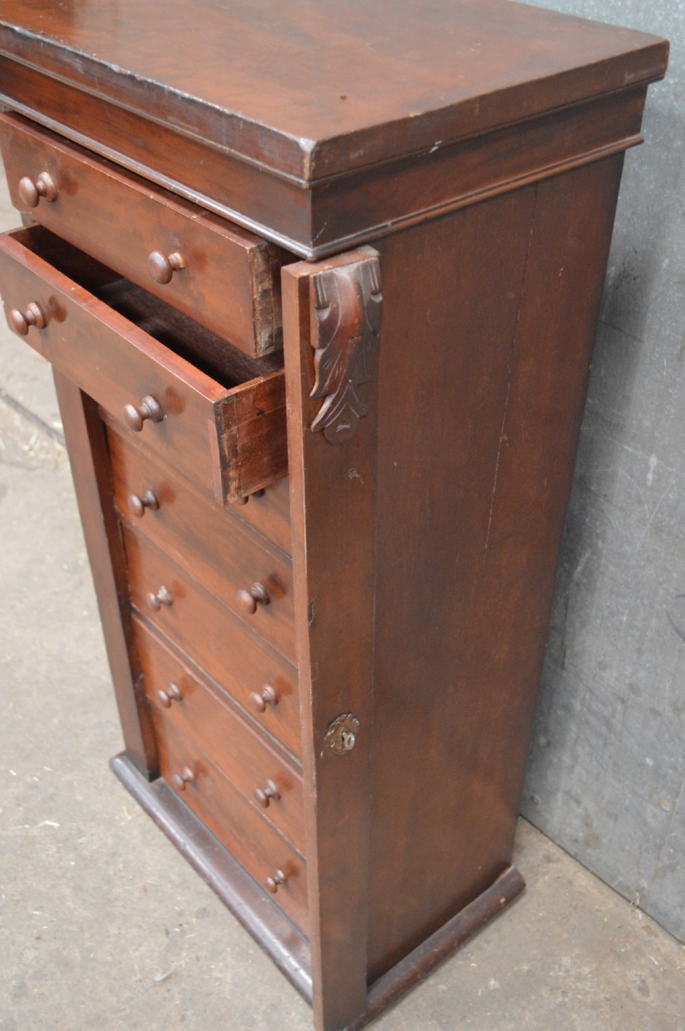 A tall, narrow Victorian mahogany Wellington chest featuring seven graduated drawers with turned wooden knobs and a hinged right-hand locking bar. View IV