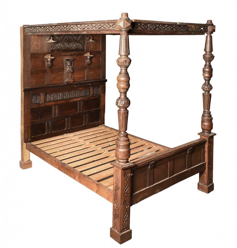 An early 19th-century carved oak four-poster bed frame featuring turned front posts, a carved panelled headboard, and an upper canopy structure.