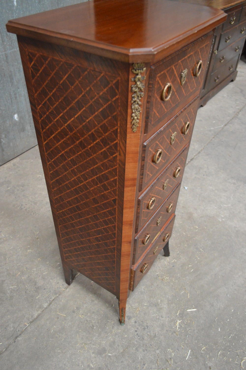 A tall, narrow 19th-century French timber chest featuring five drawers with geometric diamond parquetry inlay, brass ring handles, ornate keyhole escutcheons, and gilded corner mounts. View III
