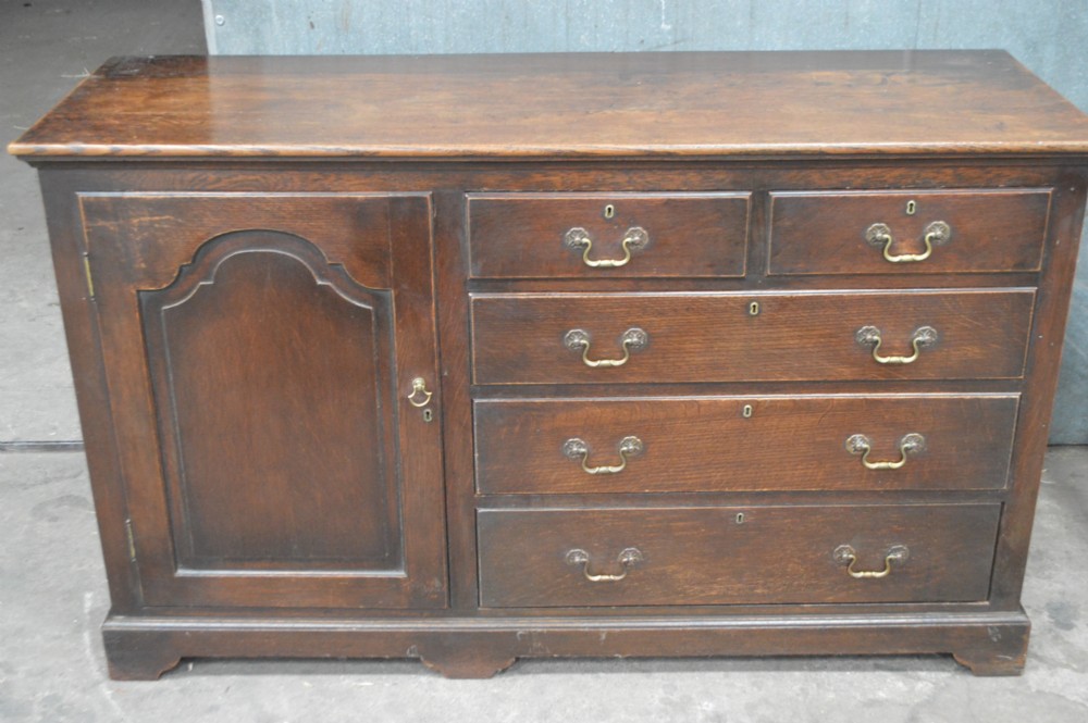 An 18th-century dark oak open-backed dresser featuring an upper plate rack with fretwork detailing positioned above a base with five drawers and an arched panelled cupboard door. View II