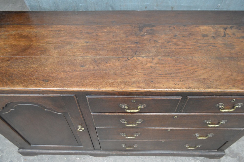 An 18th-century dark oak open-backed dresser featuring an upper plate rack with fretwork detailing positioned above a base with five drawers and an arched panelled cupboard door. View III