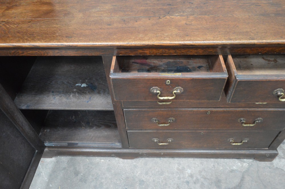An 18th-century dark oak open-backed dresser featuring an upper plate rack with fretwork detailing positioned above a base with five drawers and an arched panelled cupboard door. View IV