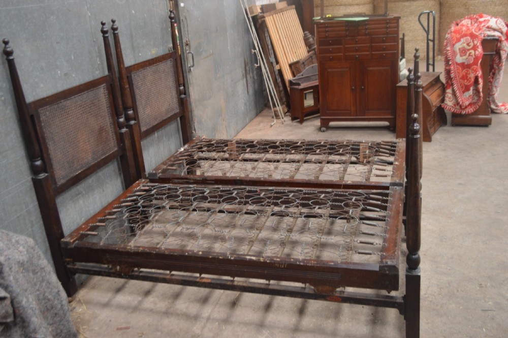 A matching pair of dark oak single bed frames featuring woven cane headboards, turned corner posts with finials, and castor wheels. View IV