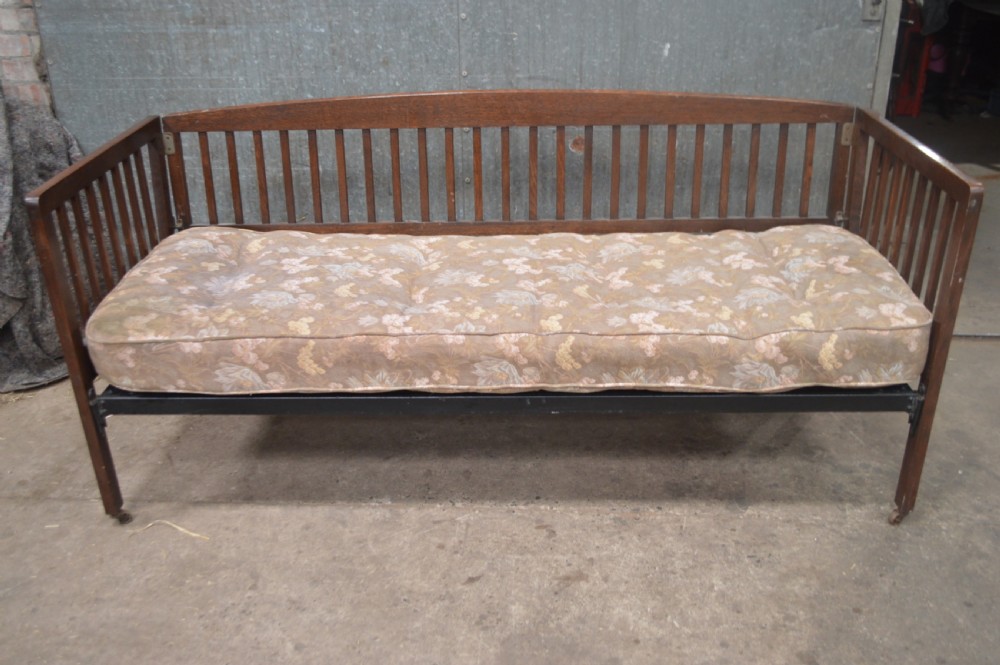 A 1920s oak day bed with vertical slatted back and side panels, fitted with a patterned floral cushion mattress.