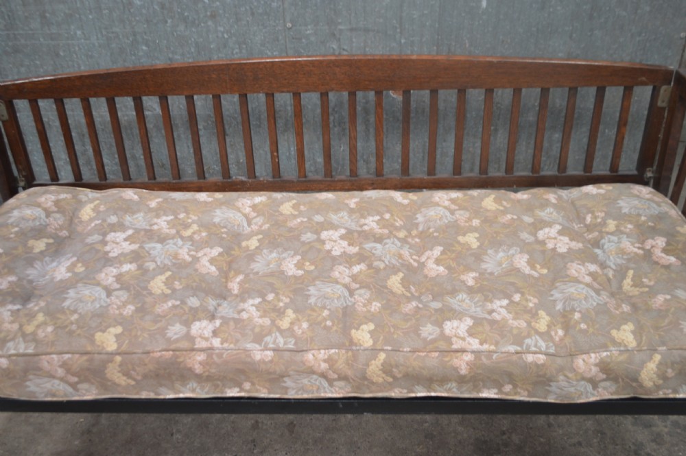 A 1920s oak day bed with vertical slatted back and side panels, fitted with a patterned floral cushion mattress. View III