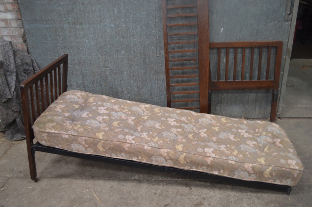 A 1920s oak day bed with vertical slatted back and side panels, fitted with a patterned floral cushion mattress. View IV