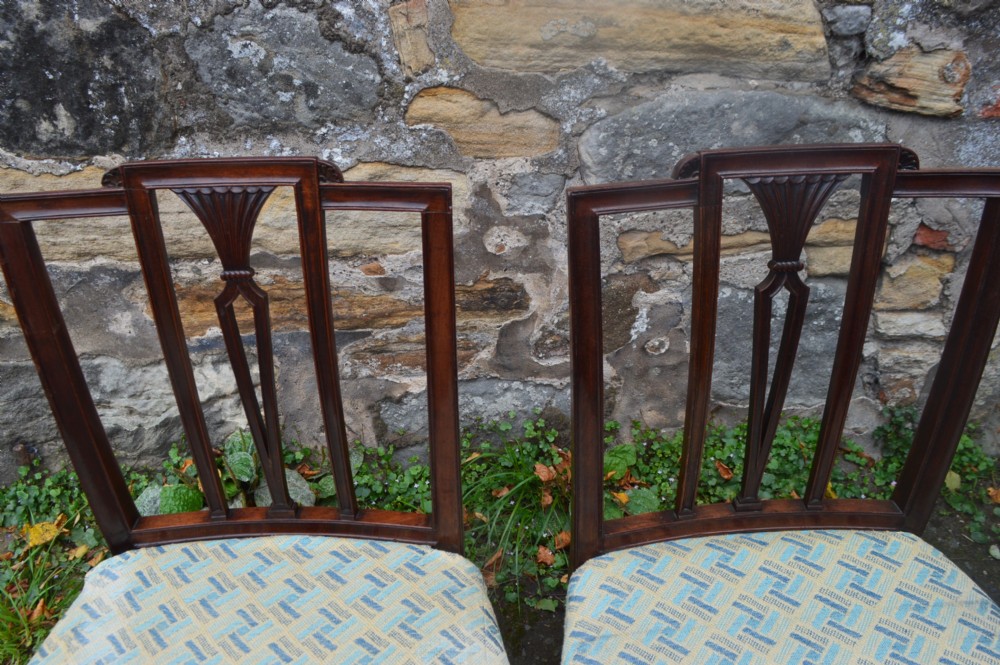 A set of twelve George III mahogany dining chairs featuring carved openwork back splats, patterned upholstery, and square tapered legs. View IV