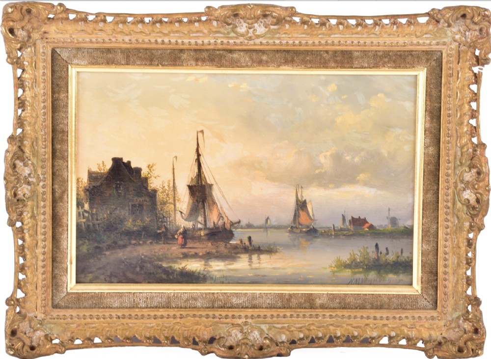 A 19th-century oil painting depicting a calm river scene with sailing boats, a cottage, and a soft sky, enclosed in an ornate gilded frame with a velvet slip.
