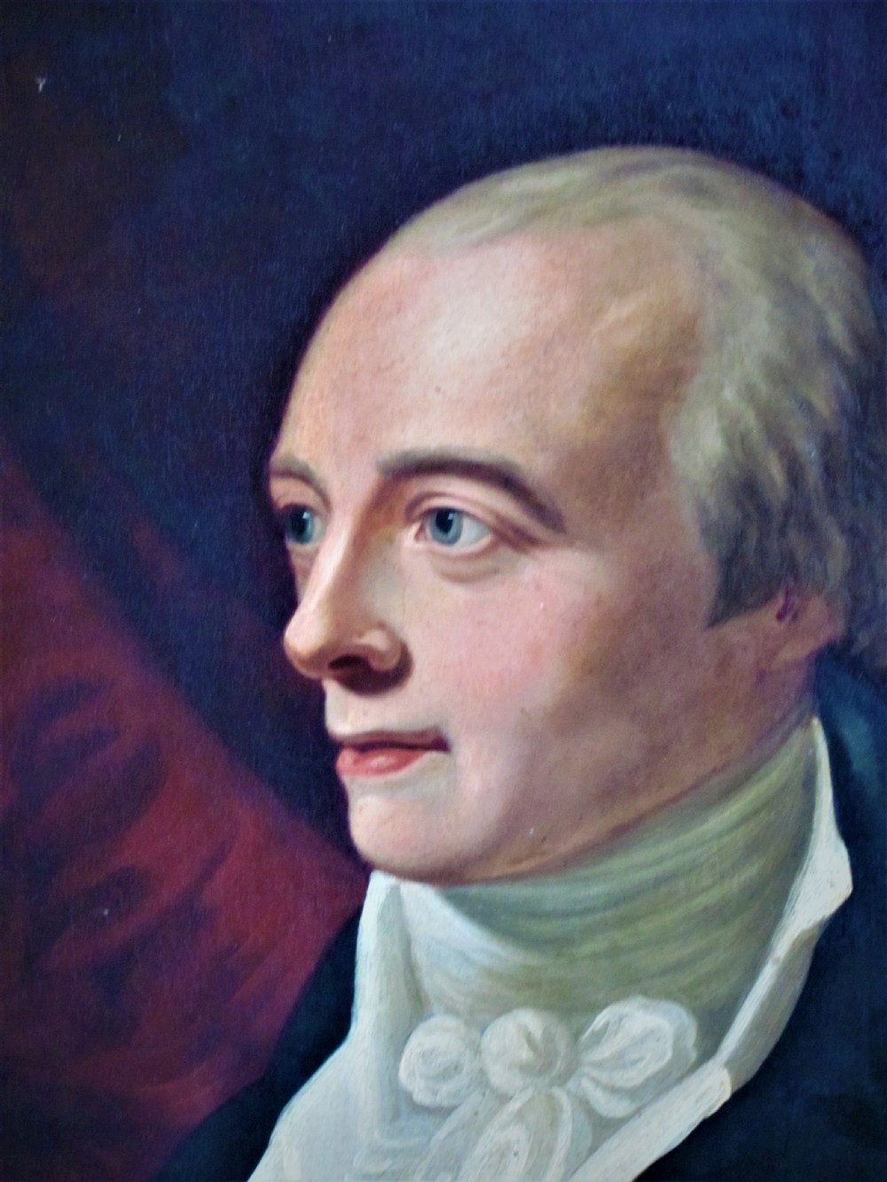 A 19th-century framed oil painting depicting a gentleman in a dark blue coat and white cravat set against a red draped backdrop. View II