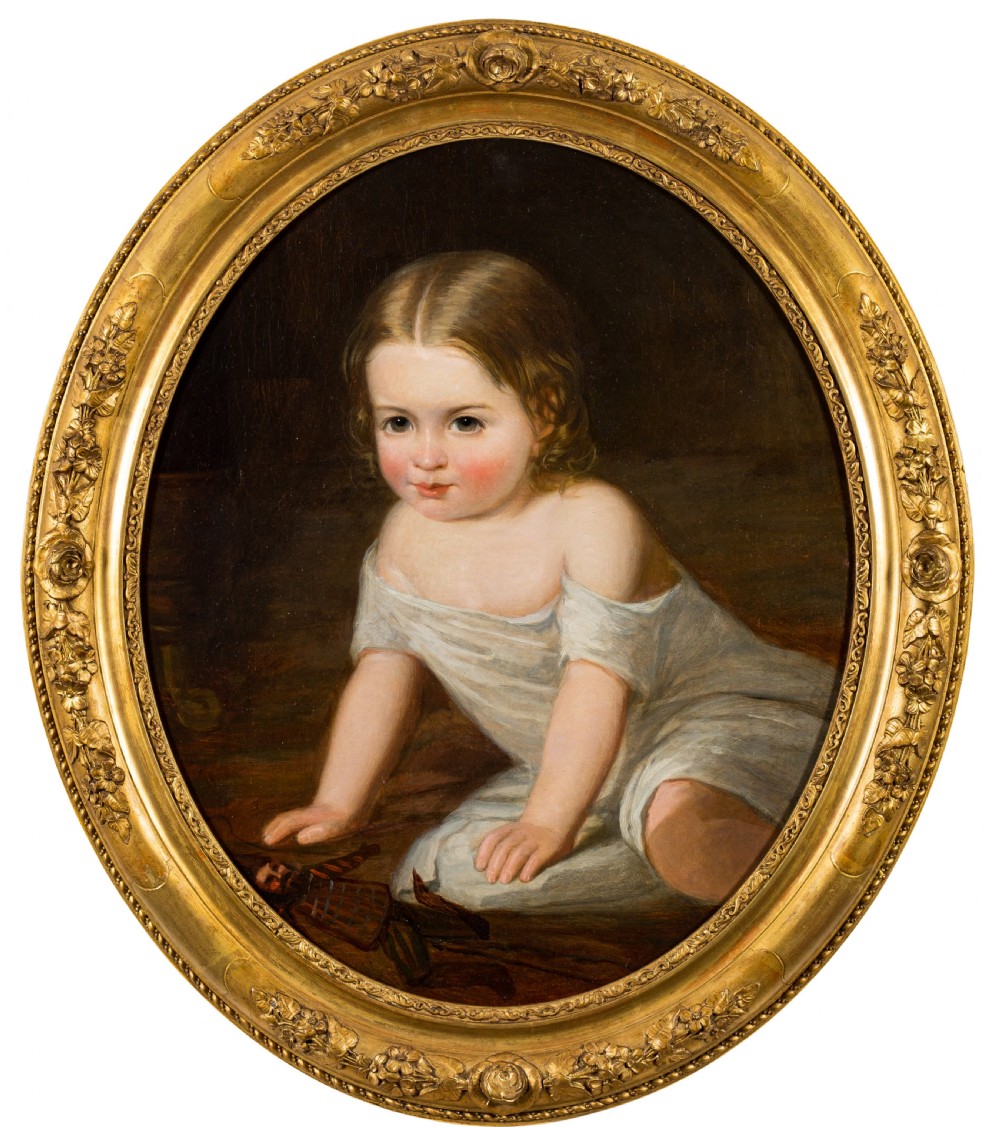 An oval Victorian oil painting depicting a young child in a white dress seated on the floor with a toy, enclosed within a carved giltwood frame.