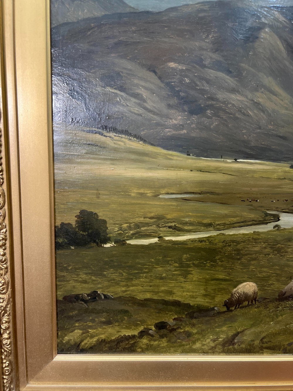 An oil painting depicting sheep grazing in a green valley before mountains, framed in an ornate gilded frame. View IV