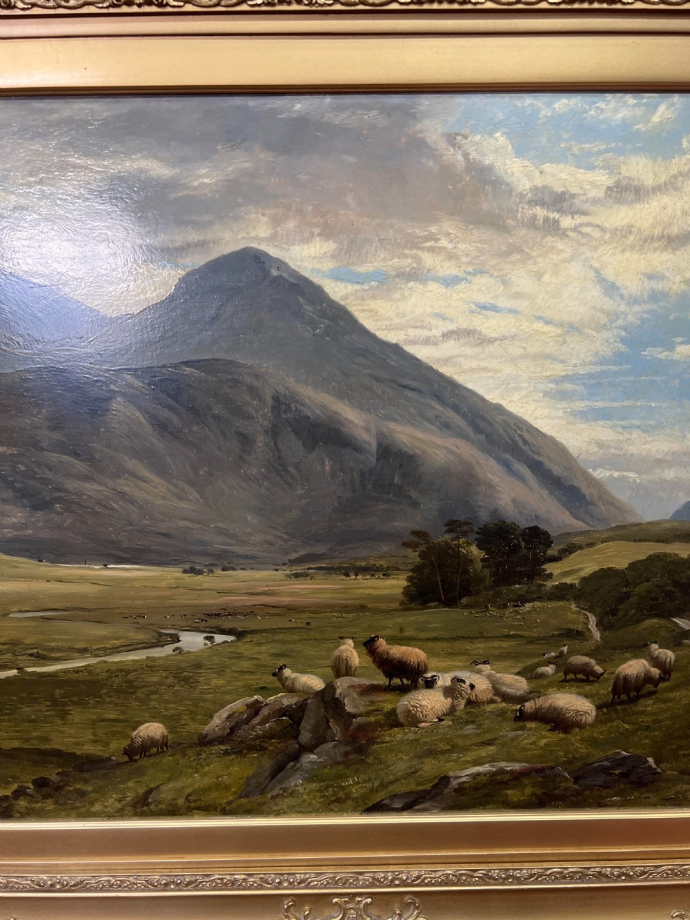 An oil painting depicting sheep grazing in a green valley before mountains, framed in an ornate gilded frame. View VII