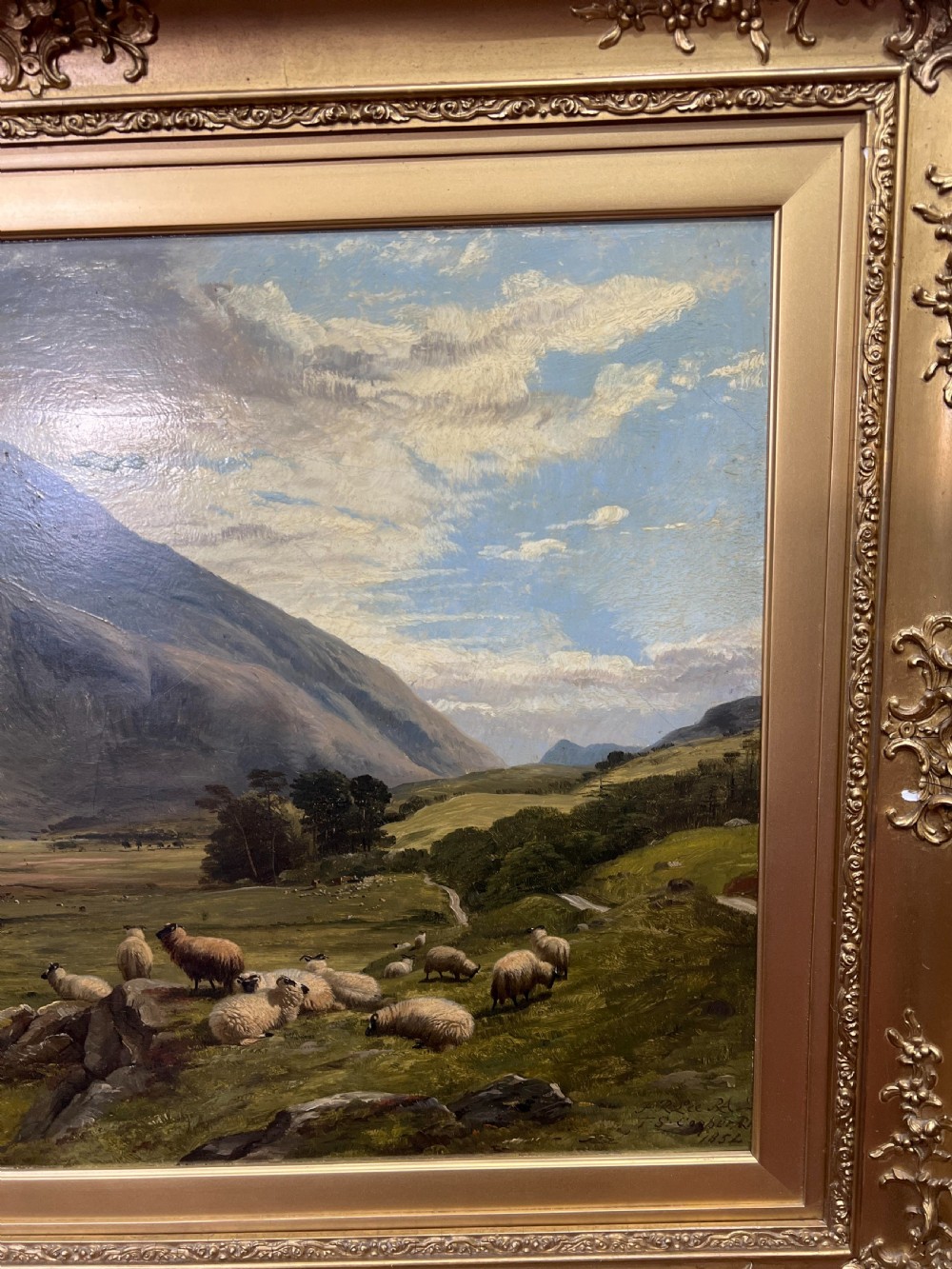 An oil painting depicting sheep grazing in a green valley before mountains, framed in an ornate gilded frame. View VIII
