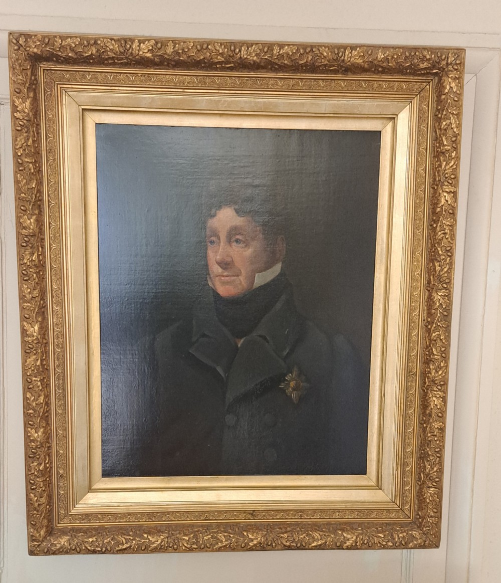 A 19th-century oil painting depicting a gentleman in a dark double-breasted jacket and white cravat, set within an ornate gilt frame decorated with oak leaf mouldings.
