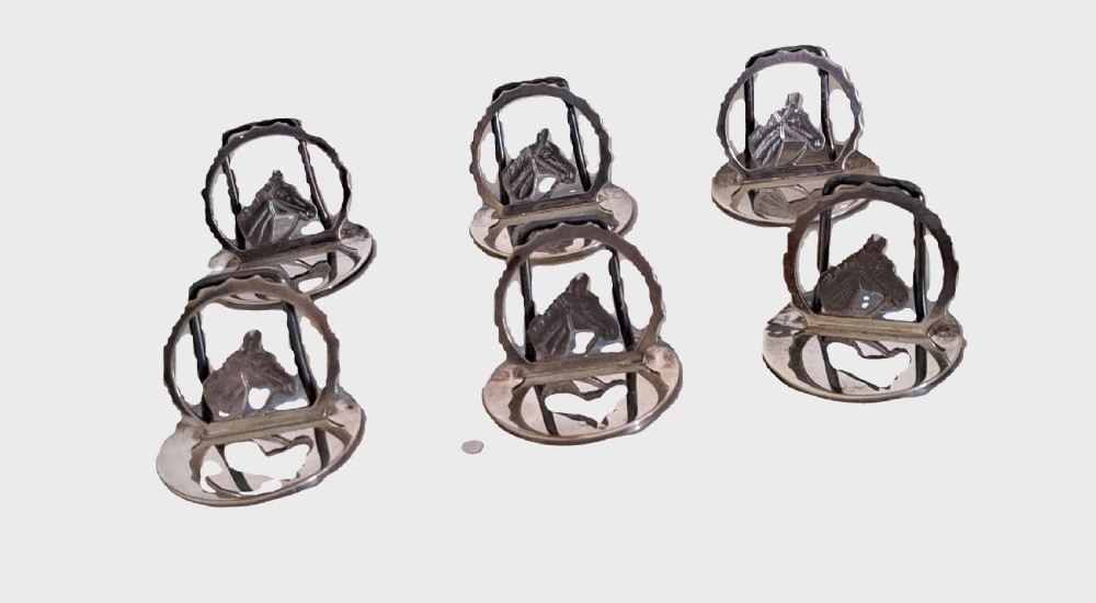 A set of six silver-toned place card holders featuring cast horse heads framed within arched rings on round bases.