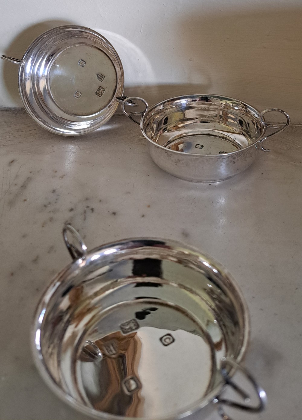 A set of four small, round sterling silver wine tasters with twin loop handles and visible hallmarks stamped on the polished interiors. View III