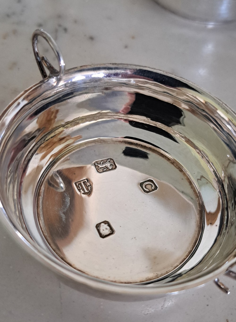 A set of four small, round sterling silver wine tasters with twin loop handles and visible hallmarks stamped on the polished interiors. View IV