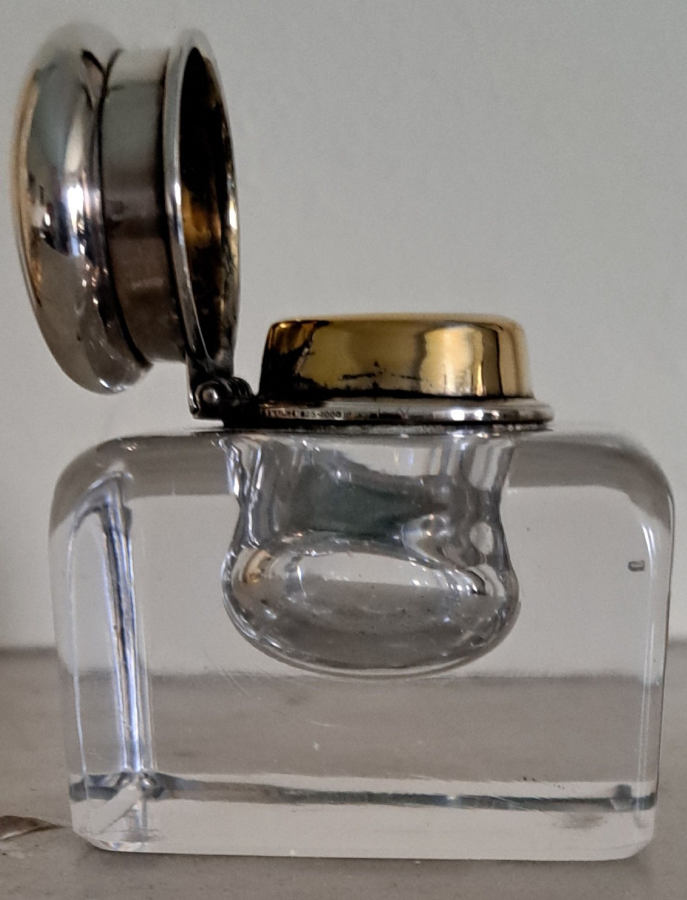 A square clear glass inkwell featuring a hinged silver dome lid with a gilded interior mechanism. View III