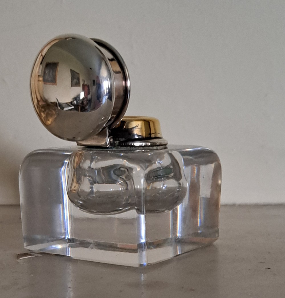 A square clear glass inkwell featuring a hinged silver dome lid with a gilded interior mechanism. View V