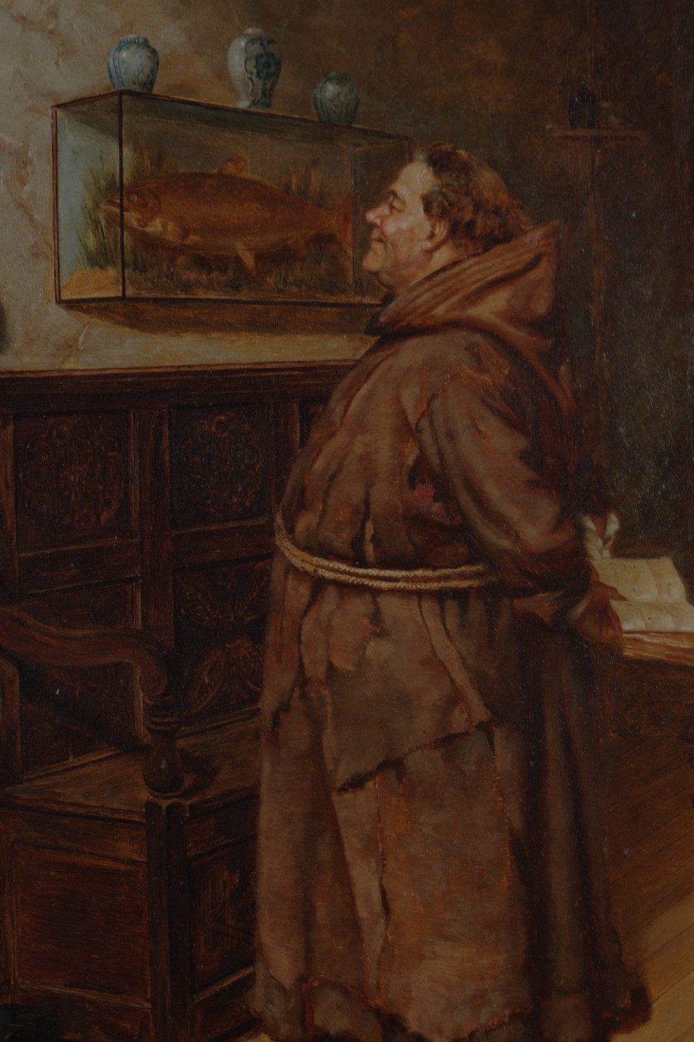 A 19th-century framed oil painting depicting a monk in a brown robe looking at a mounted fish in a glass display case. View IV