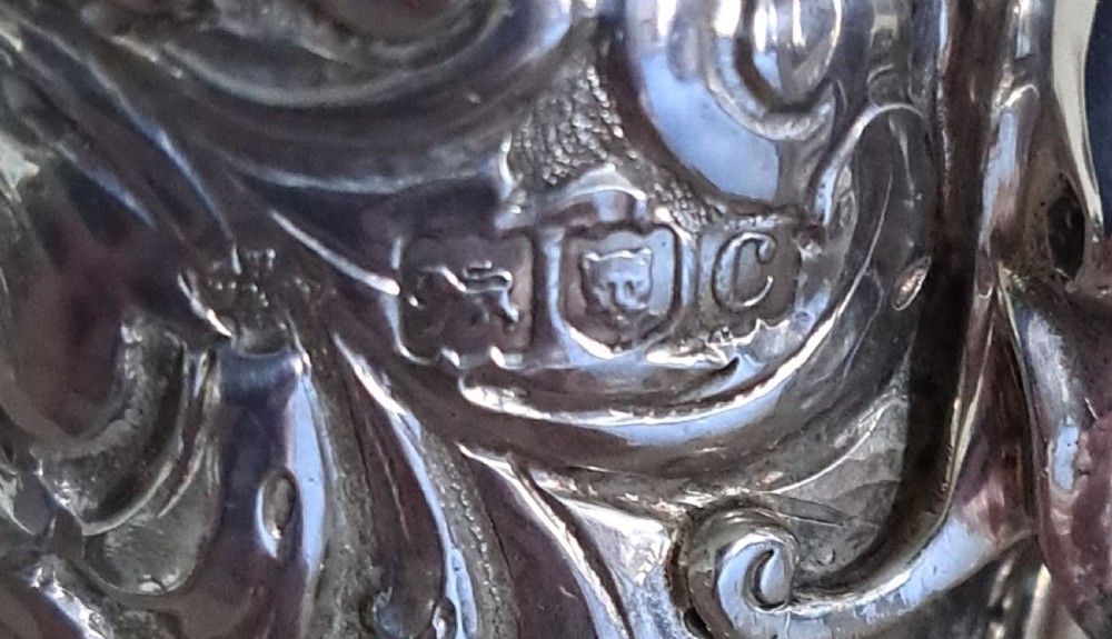 A Victorian sterling silver sugar caster shaped like a cornucopia horn, decorated with intricate repousse floral scrollwork, a perforated removable lid, and standing on a tripod base. View VI