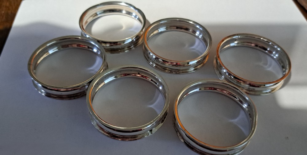 A set of six Victorian sterling silver napkin rings displayed inside a black fitted presentation box lined with silk and purple velvet. View VI